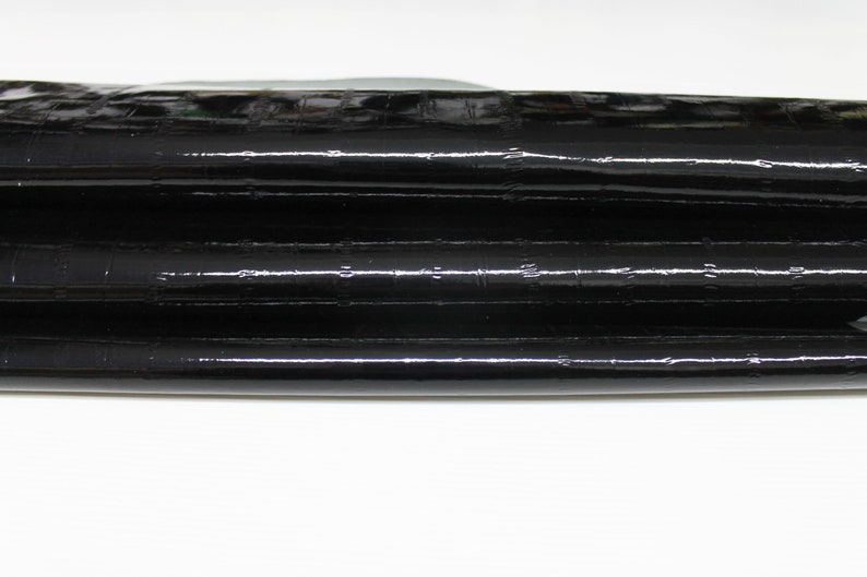 May include: Black leather with a textured, crocodile-like pattern. The leather is folded in thirds.