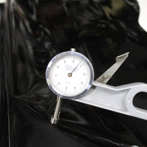 May include: A close-up of a dial gauge measuring the thickness of a black material. The gauge reads 0.17 mm and is labeled "GALAI" Made in USA.