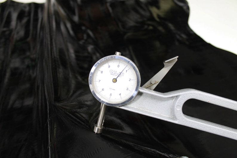 May include: A close-up of a dial gauge measuring the thickness of a black material. The gauge reads 0.17 mm and is labeled "GALAI" Made in USA.