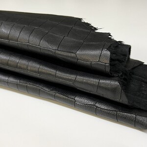 May include: Black leather with a crocodile embossed pattern. The leather is folded in thirds and has a frayed edge. The label "ITALIAN SKINS" is visible in the top left corner.