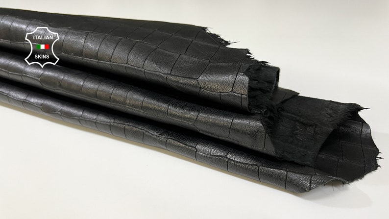 May include: Black leather with a crocodile embossed pattern. The leather is folded in thirds and has a frayed edge. The label "ITALIAN SKINS" is visible in the top left corner.
