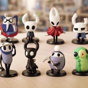 May include: A collection of eight character figurines, each with a unique design and color scheme. The figures are set on black circular bases. The characters include a variety of shapes and colors, such as white, black, blue, red, and green.