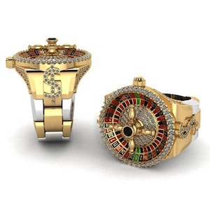 May include: A gold ring with a roulette wheel design, featuring red, black, and green sections. The ring has a dollar sign detail and is embellished with small, clear stones, giving it a luxurious look.