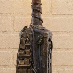 Peut inclure: Lampe de table originale fabriquée à partir d'une bouteille recyclée, avec une ampoule chaleureuse et brillante. La lampe est ornée de touches de clavier et d'éléments métalliques, créant une esthétique industrielle et steampunk. La lampe mesure environ 30 cm de haut.