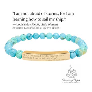May include: A turquoise beaded bracelet with a gold-colored bar featuring an engraved quote from Louisa May Alcott's "Little Women." The quote reads, "I am not afraid of storms, for I am learning how to sail my ship."