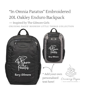May include: A black 20L Oakley Enduro backpack featuring white embroidery of an umbrella and the text In Omnia Paratus and Rory Gilmore. The design includes a top handle, zippered compartments, and side mesh pockets for storage and organisation.
