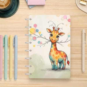 May include: A disc-bound notebook featuring a colorful illustration of a giraffe with large eyes holding a thin branch in its mouth, set against a light background with scattered pastel-colored circles and a soft green ground area.