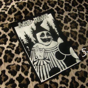Op de afbeelding: Een rechthoekige zwart-witte stoffen patch met een grafische illustratie van een clown met een puntmuts en een gestreepte kraag. De tekst "ACID BATH" is in een gestileerd lettertype bovenaan gedrukt. Het ontwerp bevat donkere bomen.