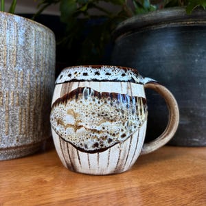 Bruin-crème keramische mok met reactief glazuur, handgemaakte aardewerk koffiekop, rustiek aardewerk in aardetinten, hippe keukendecoratie.