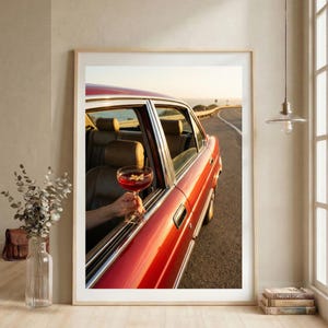 以下が含まれることがあります： 窓からカクテルを持った赤いヴィンテージカーの額入りプリント。車は、背景に海がある海岸道路を走行しています。車の内装は茶色の革張りのシートです。