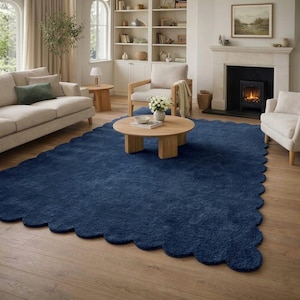 Könnte beinhalten: Ein großer, marineblauer Teppich mit gewelltem Rand in einem Wohnzimmer. Der Teppich liegt auf einem Holzboden, mit neutralfarbenen Möbeln wie Sofa, Stühlen und einem Couchtisch. Ein Kamin und Bücherregale sind im Hintergrund zu sehen.
