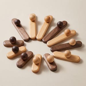 May include: A collection of wooden bottle stoppers in various shades of brown and natural wood tones. Each stopper features a small, round ball on top of a rectangular base. The stoppers are arranged in a circular pattern.