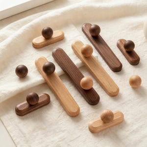May include: Wooden drawer pulls in various shades of brown. The pulls feature a rounded knob on a rectangular base. The wood tones range from light to dark, with some pulls having a natural wood grain.