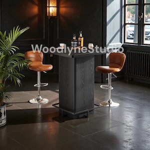 May include: A black wooden bar table with a square top and a central support, paired with two brown leather bar stools. The table has a footrest and is set against a dark wall with a window.