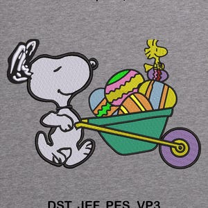 May include: Embroidered design of Snoopy pushing a wheelbarrow of colourful Easter eggs, with Woodstock perched on top. The design includes the text "2 SIZES | 5X7, 6X10" and "DST, JEF, PES, VP3" on a grey background.