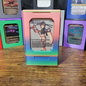 May include: A rectangular 3D-printed plastic card storage box featuring a vertical gradient of pink, orange, yellow, green, and blue. The front has a cutout window displaying a Yuffie Kisaragi trading card with text including Legendary Creature.