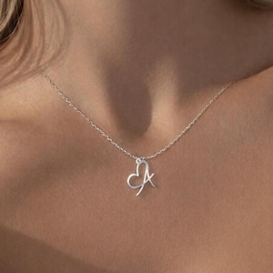 May include: A silver necklace with a heart-shaped pendant and the letter "A". The pendant is attached to a delicate chain. The necklace is worn around the neck.