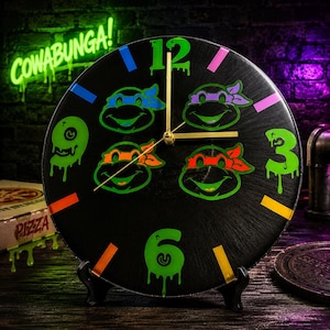 May include: A circular black wall clock featuring four cartoon turtle faces with blue, purple, orange, and red masks. The clock face displays neon green numbers 12, 3, and 6 with a dripping effect, gold hands, and colorful rectangular hour markers.