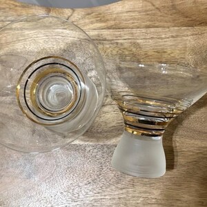 May include: Two clear glass martini glasses with gold and black spiral detailing. One glass is a wide, shallow bowl, and the other has a conical bowl atop a frosted base. The glasses are designed for cocktails.