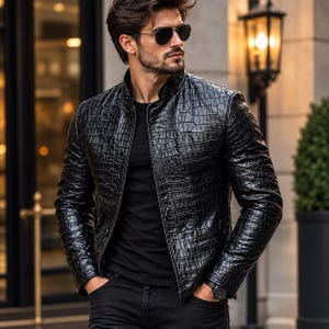 May include: A black jacket with a textured crocodile skin pattern, featuring a high collar and a front zipper closure. The jacket is worn over a plain black t-shirt and paired with black trousers. Dark sunglasses are worn on the face.