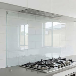 Peut inclure: Une crédence de cuisine en verre transparent installée au-dessus d'une table de cuisson à gaz en acier inoxydable. La crédence est fixée sur un mur carrelé blanc. Une hotte aspirante en acier inoxydable est au-dessus.