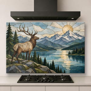 Puede incluir: Un cuadro rectangular con una ilustración estilo vidriera de un alce sobre un acantilado rocoso frente a un lago, pinos y montañas nevadas bajo un sol dorado, montado sobre una estufa de cocina de color negro.