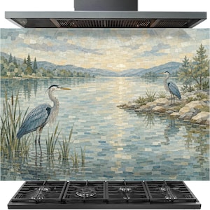 May include: A rectangular kitchen splashback panel featuring a mosaic-style landscape illustration of a lake at sunset. Two blue-grey herons stand in the foreground among reeds and rocky shores, with distant mountains under a pale, cloudy sky.