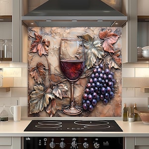Op de afbeelding: Decoratieve keukenachterwand met een wijnglas gevuld met rode wijn, een tros druiven en wijnbladeren. Het kunstwerk heeft een textuur, driedimensionale uitstraling met bruine, rode en paarse tinten. De achterwand is geïnstalleerd boven een zwarte kookplaat.