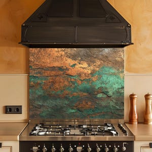 May include: A kitchen backsplash with a textured, stone-like appearance. The color palette includes shades of brown, copper, and green, creating a rustic and natural aesthetic. The backsplash is installed above a stainless steel gas hob.