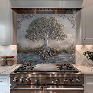 May include: A decorative kitchen backsplash features a detailed relief of a tree with exposed roots and a full canopy. The artwork is set against a backdrop of a river and sky, framed by ornate silver trim. The backsplash is mounted above a stainless steel range.