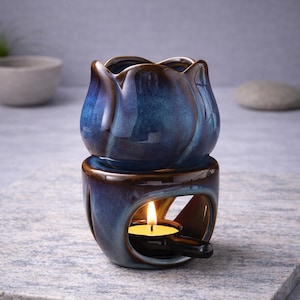 Peut inclure: Diffuseur d'huiles essentielles en céramique bleue et marron en forme de fleur. La partie supérieure est un bol en forme de fleur, et la base a une ouverture pour une bougie chauffe-plat. Une bougie allumée est à l'intérieur.