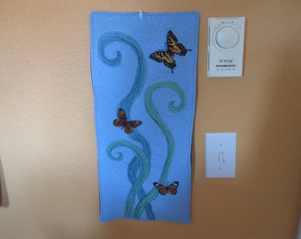 May include: A blue fabric wall hanging with a design of green vines and butterflies. The butterflies are brown and orange with black markings.
