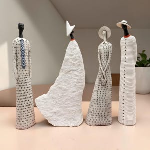 Op de afbeelding: Vier abstracte keramische beeldjes. Eén figuur draagt een pak met een stropdas, een ander een witte jurk, een derde een jurk met een kleine handtas en de laatste een jas met een hoed. De figuren zijn voornamelijk wit met zwarte accenten.
