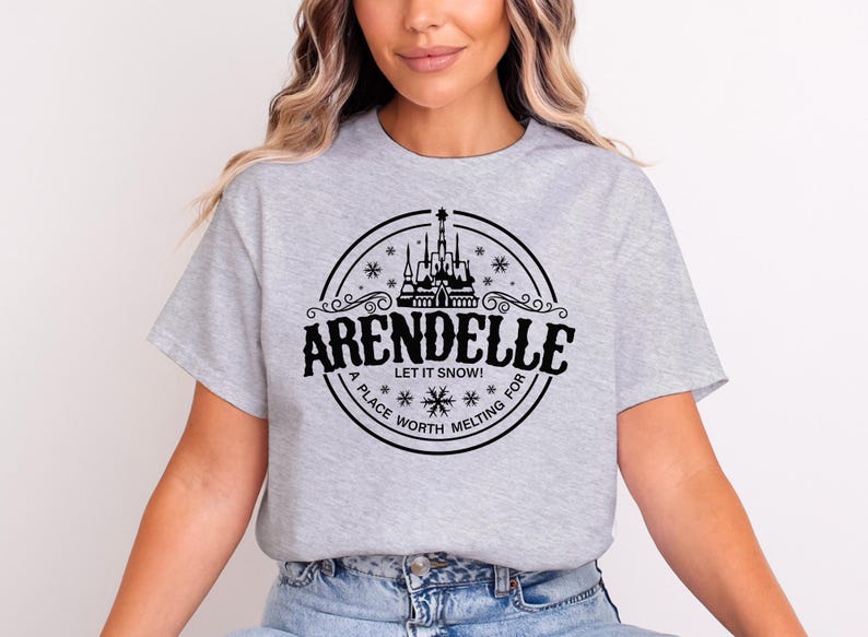 May include: A light gray t-shirt featuring a black circular design with the word "ARENDELLE" and the phrase "LET IT SNOW!" The design includes a castle, snowflakes, and the words "A PLACE WORTH MELTING FOR".