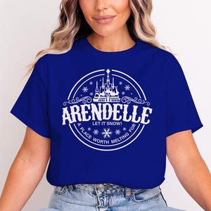 May include: Royal blue t-shirt featuring a white circular graphic with the word "ARENDELLE" above "LET IT SNOW!" and "A PLACE WORTH MELTING FOR". The graphic includes a castle and snowflakes.