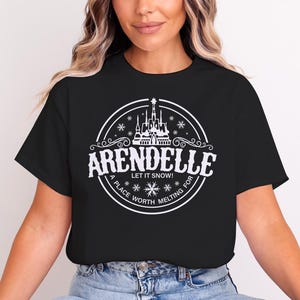 May include: Black t-shirt with a white circular graphic featuring the word "Arendelle" and a castle illustration. The text "Let it snow!" and "A place worth melting for" are also included in the design.
