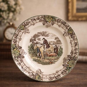 Może przedstawiać: Ozdobny ceramiczny talerz z centralną sceną pasterską, przedstawiającą postacie na koniach i psy. Obrzeże zdobi wzór winogron i winorośli w odcieniach brązu i zieleni. Talerz ma zieloną obwódkę.
