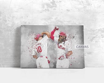 May include: Canvas print featuring a watercolor style illustration of two baseball players in Phillies uniforms celebrating a play. The players are wearing red helmets and white and red striped jerseys. The word "Canvas" is printed on the bottom right.