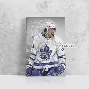 Könnte beinhalten: Leinwanddruck eines Hockeyspielers in einem weiß-blauen Trikot der Toronto Maple Leafs. Das Kunstwerk zeigt eine stilisierte, actionorientierte Darstellung mit Farbspritzereffekten. Das Wort "CANVAS" ist sichtbar.