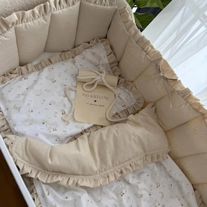 Puede incluir: Una cuna beige con un interior suave y acolchado y ribete con volantes. La cuna está llena de un juego de mantas y almohadas estampadas con un diseño de pato. Se incluye una pequeña bolsa con texto.