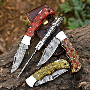 May include: Four folding knives with Damascus steel blades and patterned handles. One knife has a red and black woven handle, one has a blue and black handle, one has a red and yellow checkered handle, and one has a yellow and black woven handle.