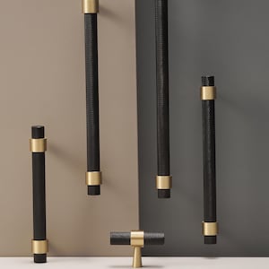 May include: A collection of black and gold cabinet hardware, including various sizes of bar pulls and a T-knob. The black pulls have a textured surface and are accented with gold-colored bands. The Modern Brass logo is visible at the bottom.