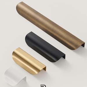 Op de afbeelding: Vier moderne messing kastgrepen in verschillende afwerkingen: antiek messing, mat zwart, goud en wit. De grepen zijn gebogen met een lip. Het Modern Brass Home Hardware logo is zichtbaar.