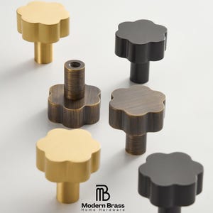 May include: A collection of flower-shaped cabinet knobs in various finishes, including gold, black, and bronze. The knobs have a modern design and are made of metal. The Modern Brass Home Hardware logo is visible.