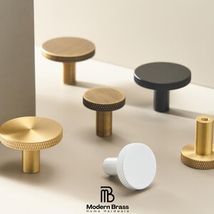 May include: A collection of modern brass cabinet knobs in various sizes and finishes. The knobs are gold, black, and white, with textured and smooth surfaces. The logo "Modern Brass Home Hardware" is visible.