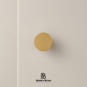 Brushed brass knob set displayed on a white architectural block to show various diameters.