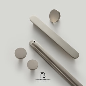 May include: A collection of modern, brushed nickel cabinet hardware. The set includes two long, rectangular pulls, three round knobs, and a logo that reads "Modern Brass Home Hardware."