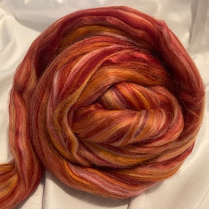 May include: A close-up of a ball of colorful wool yarn in shades of red, orange, and white. The yarn is arranged in a spiral pattern, creating a visually appealing texture.