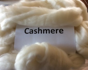 May include: A close-up of a pile of white cashmere fiber. The fiber is soft and fluffy, and the label says "Cashmere".