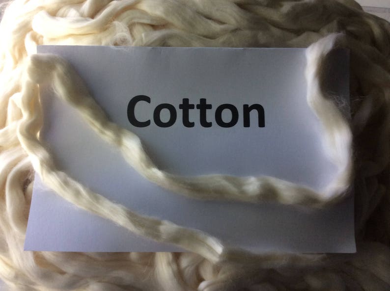 Puede incluir: Primer plano de un mont&oacute;n de fibras de algod&oacute;n blancas con una tarjeta blanca que dice "Cotton".